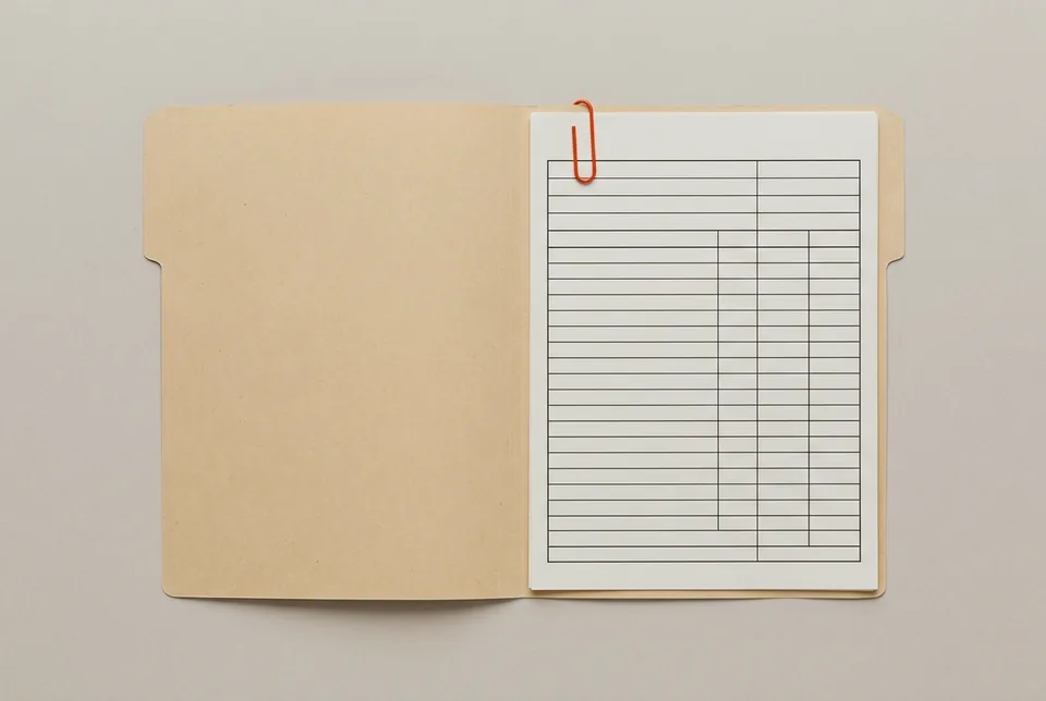 An open manila folder holding a blank ruled form, clipped with an orange-red paper clip