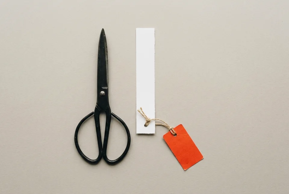 Black scissors beside a cut strip of blank paper with an orange-red tag