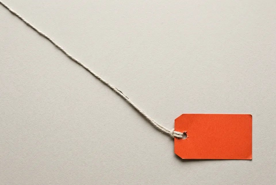 An orange-red luggage tag at the end of a long string trailing across the paper